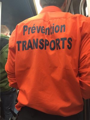 Mensch von hinten, orangenes Oberteil mit der Aufschrift „Prevention Transports“